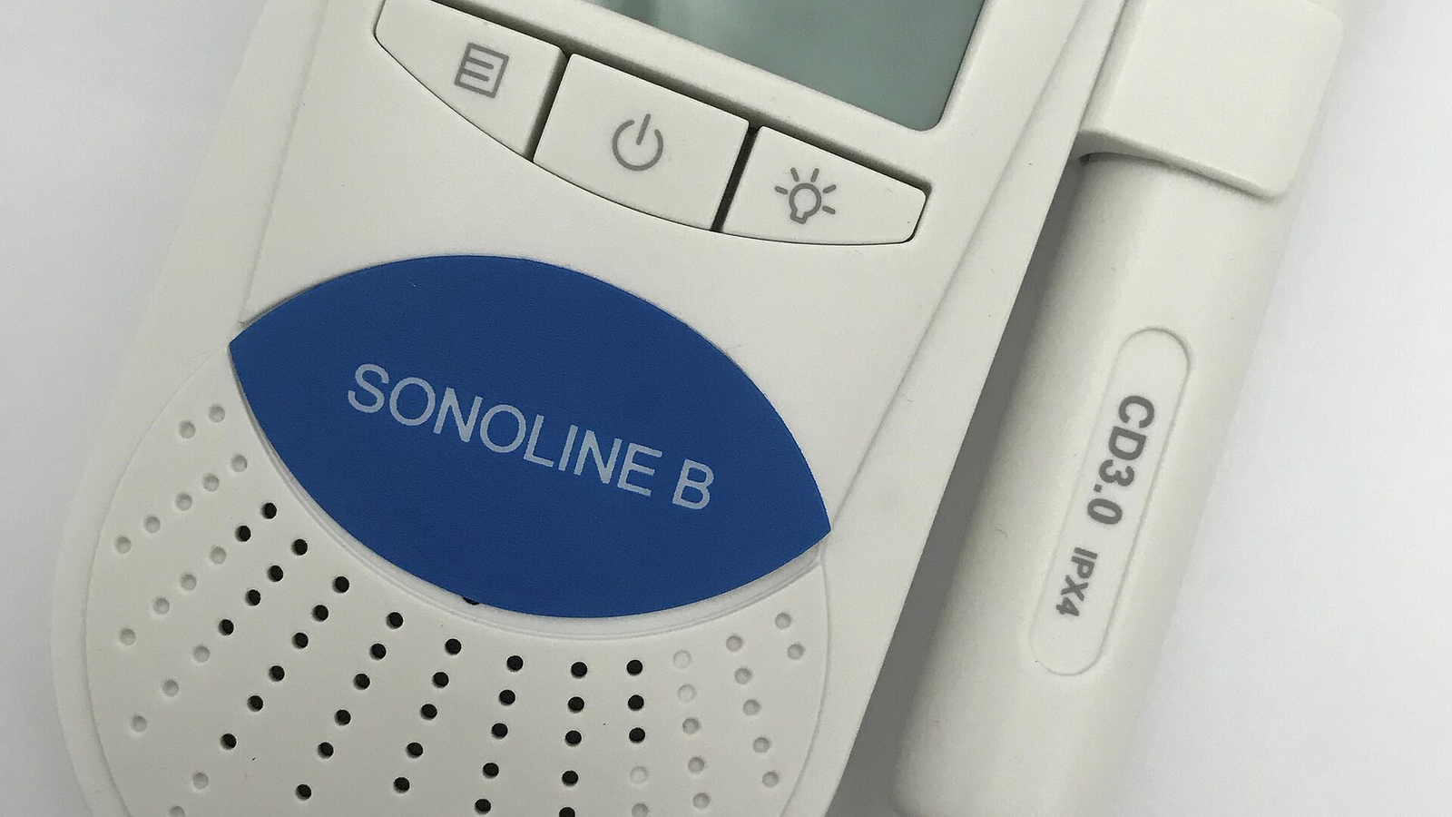 מכשיר דופלר עוברי לבן מדגם BabyDoppler Sonoline B ולצדו מתמר מחובר בכבל, מלווה מאמר של ד״ר גיא רופא